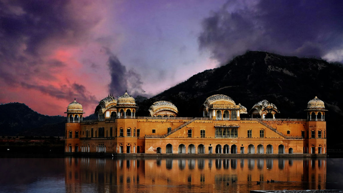 Colourful building by the water and hills, like a Rajasthan resort